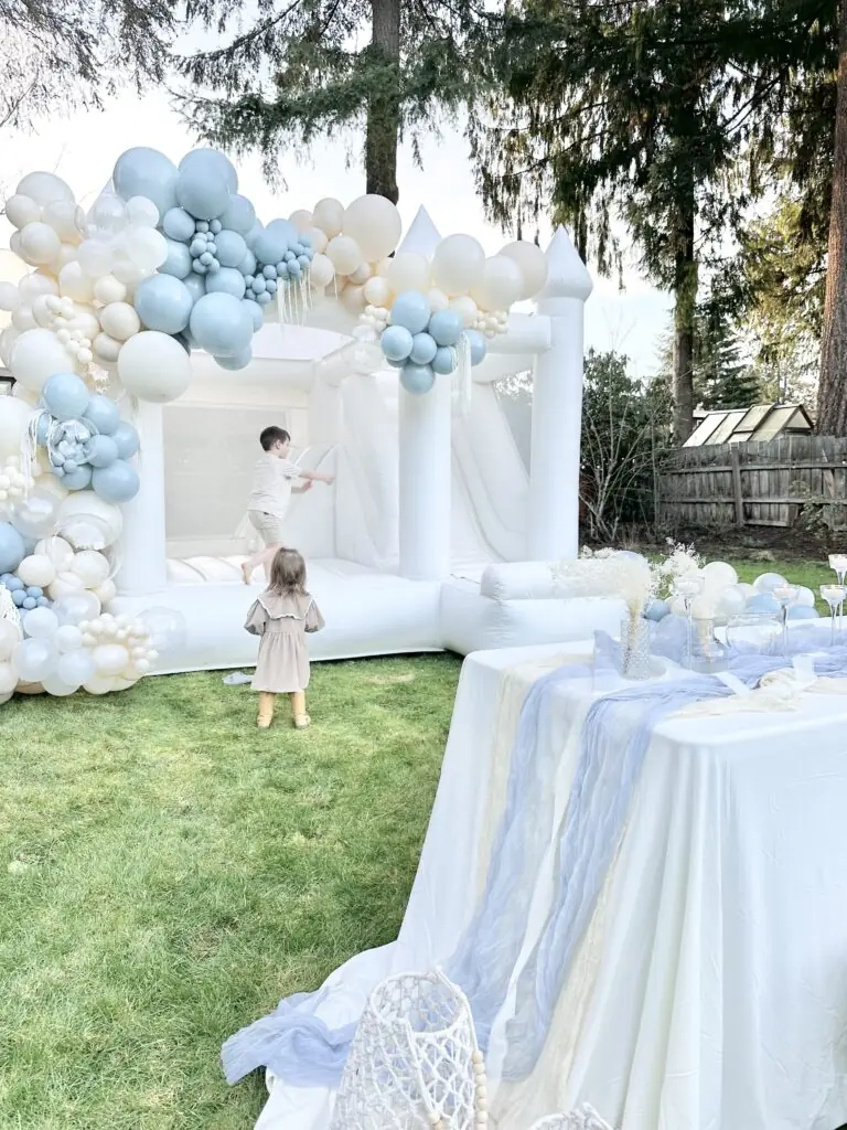 Elegant white bounce house with pastel balloon garland at backyard party, available for luxury bounce house rentals in Snohomish