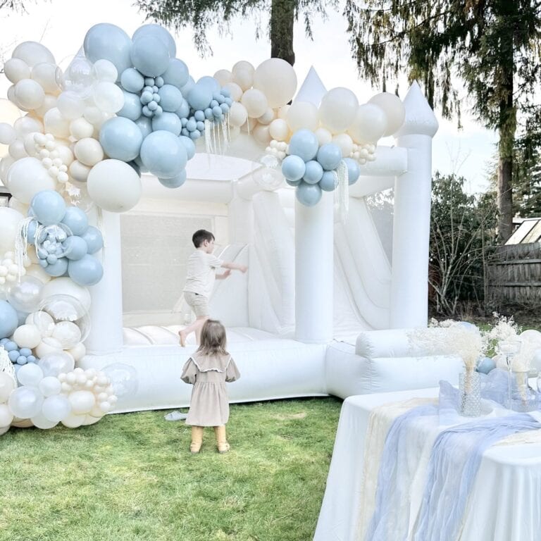 Elegant white bounce house with pastel balloon garland at backyard party, available for luxury bounce house rentals in Snohomish