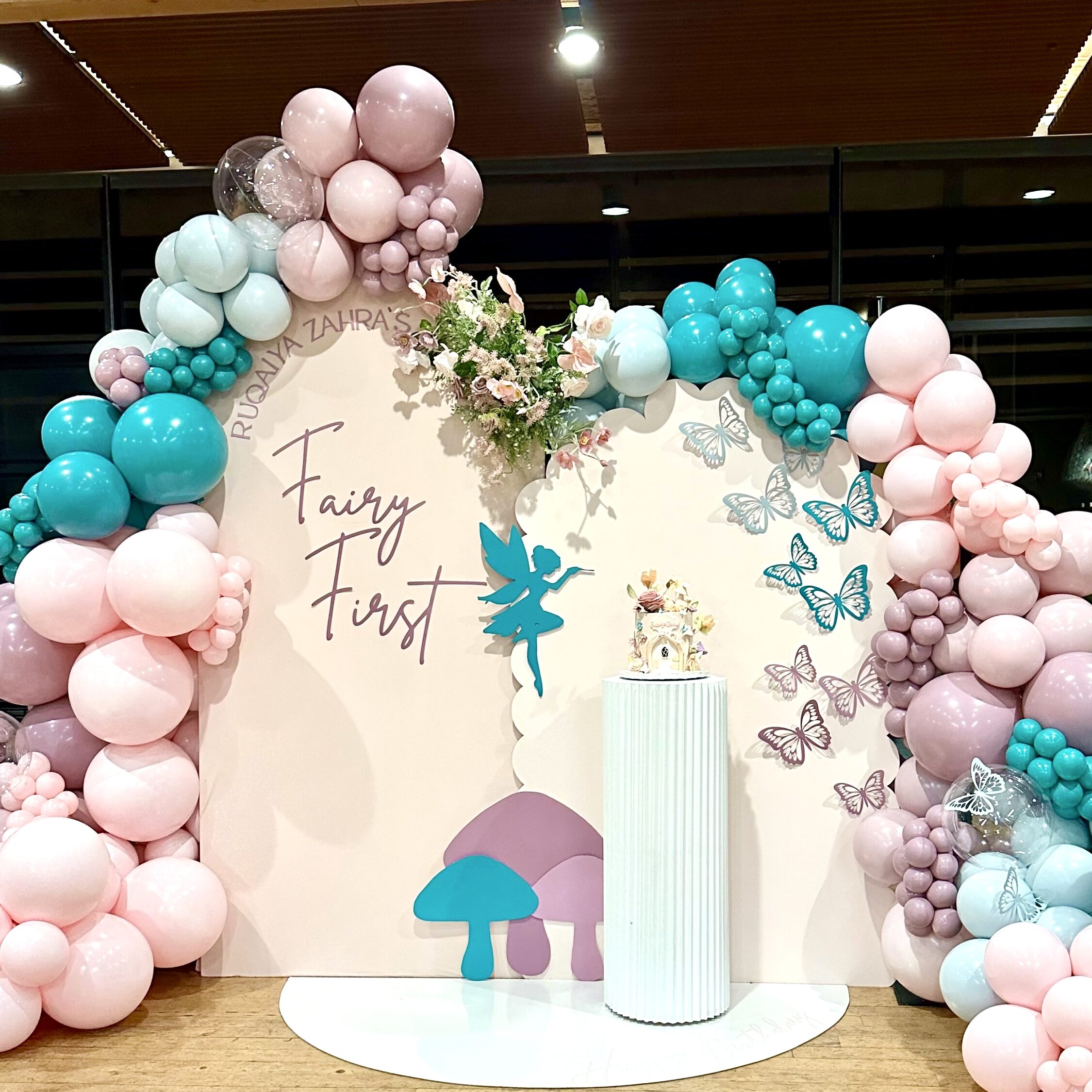 Stunning backdrop setup for instagram photos for a kids 1st birthday party in snohomish county & king county. Featuring a custom fairy prop / butterfly props, custom cake stand, backdrop arch, arched floor mat, custom vinyl signage, and balloon garlands from bradbury events.