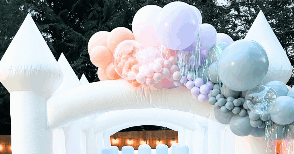 Pastel rainbow balloon garland on white bounce house / obstacle course— styled for a luxury kids’ party in marysville, WA. Includes matching heart props and iridescent fringe for a magical celebration for fun in Snohomish County.