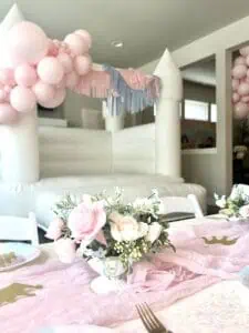 Indoor white bounce house with blush balloon garland and fringe, styled with a princess-themed kids table with petite floral arrangement & linen tabletop decor - perfect for luxury birthday parties in snohomish county & king county.