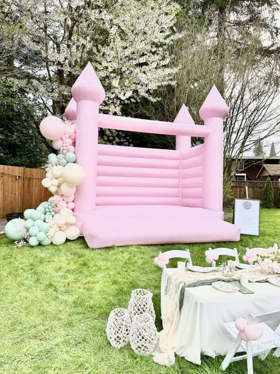 party setup with luxury bounce house rentals. Showcasing our pinkalicious pink bounce house castle, balloon garlands, stunning petite floral arrangement tabletop decor for kids seating. The perfect luxury bounce house rental in Lake Stevens