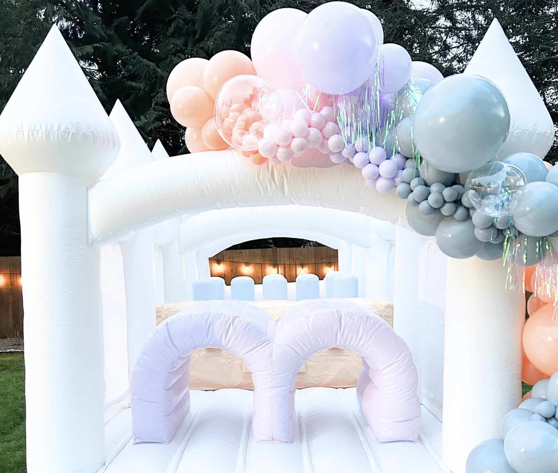 Pastel rainbow balloon garland on white bounce house / obstacle course— styled for a luxury kids’ party in Everett, WA. Includes matching heart props and iridescent fringe for a magical celebration featured as a luxury bounce house rental in Everett