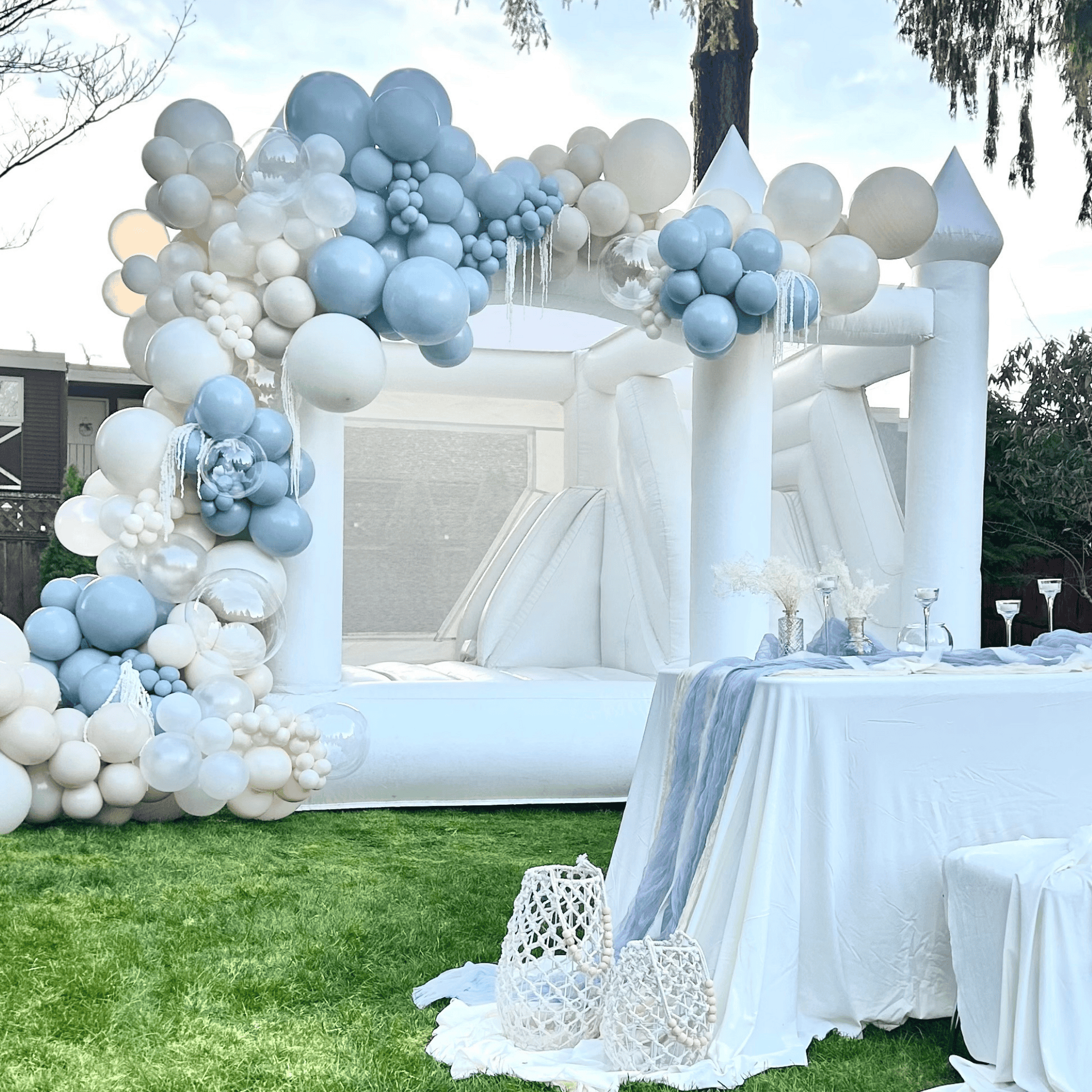 Rainier luxury white bounce house for weddings with white and blue balloon garlands, pampas accents, and table top decor.