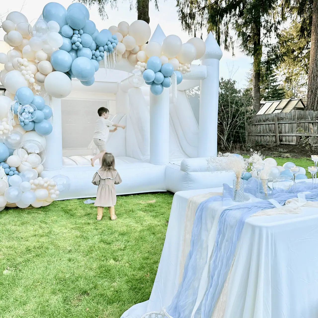 Rainier white bounce castle with an ivory and dusty blue balloon garland at an outdoor wedding in Bellevue