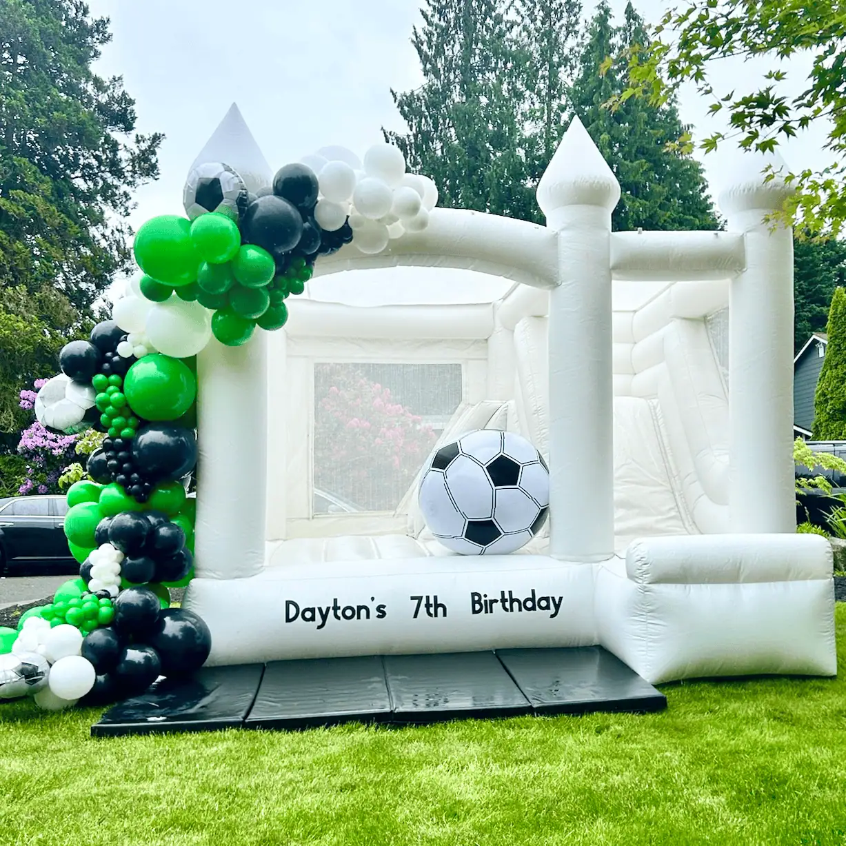 St. Helens white bounce castle with a green, black and white soccer balloon garland and a Dayton's 7th Birthday sign in Mountlake Terrace