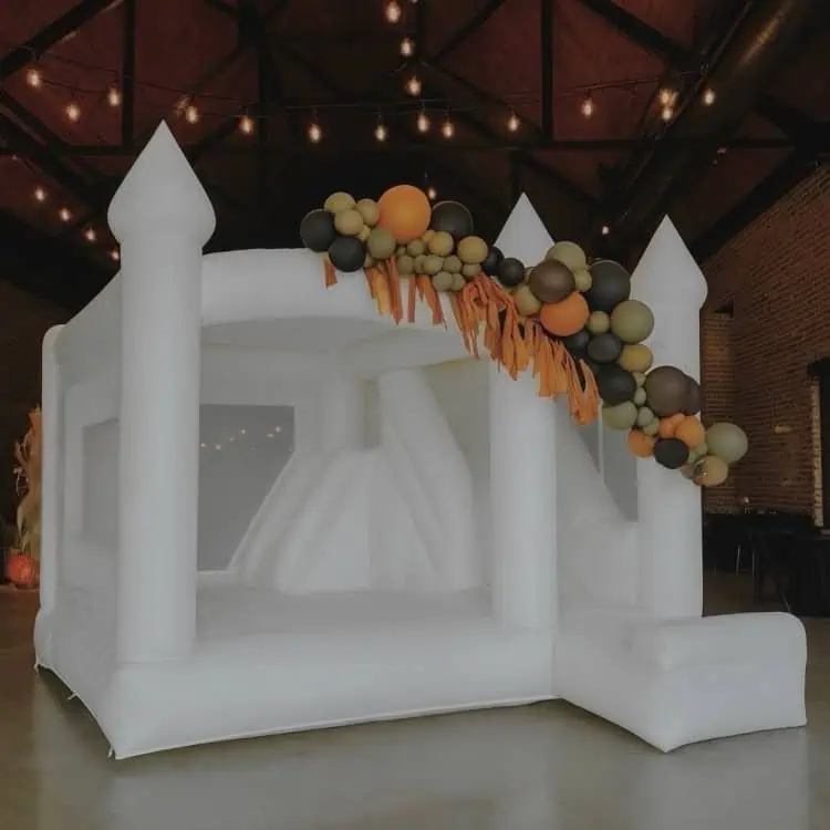 Rainier white bounce castle with an orange, olive and charcoal balloon garland and fringe at an indoor fall party