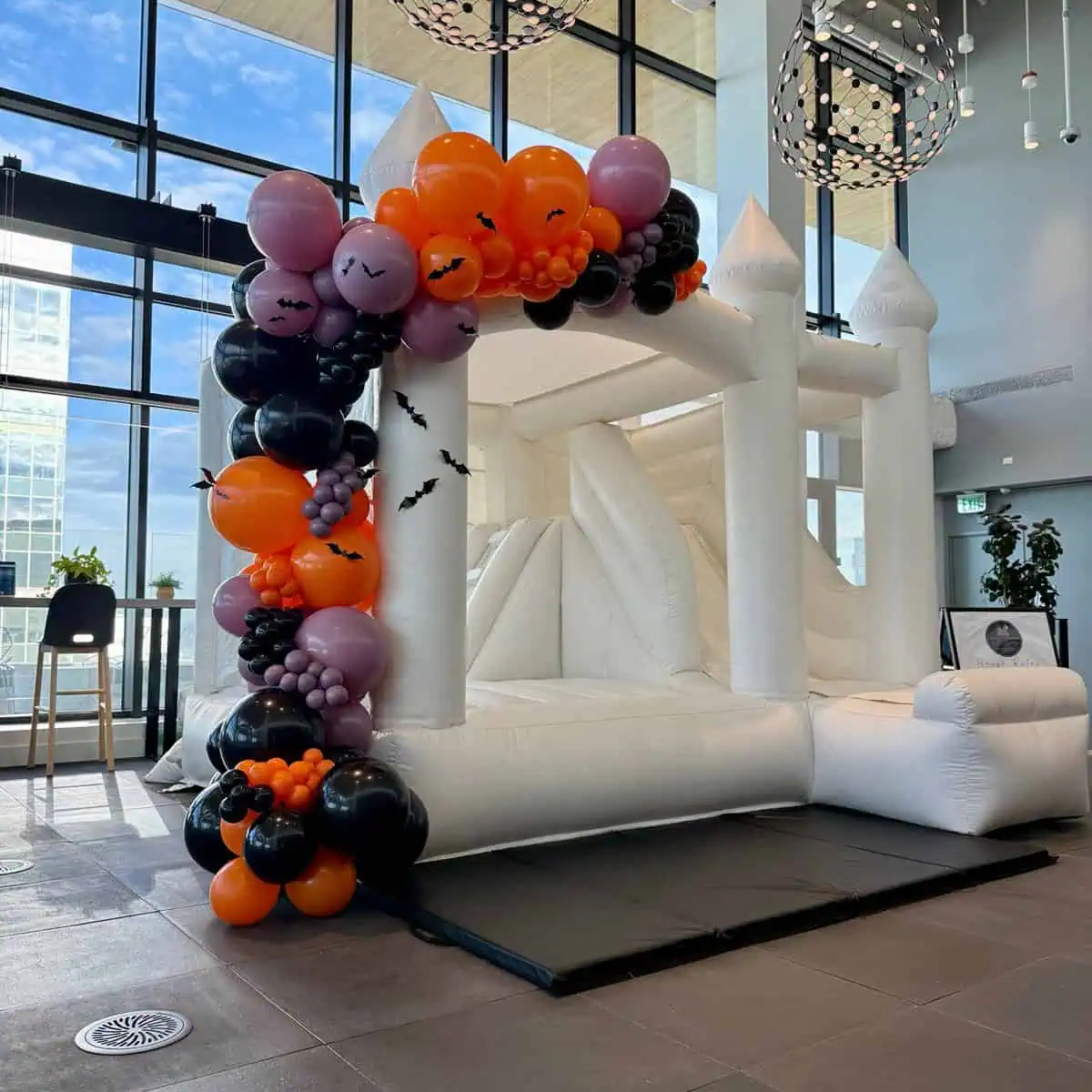 St. Helens white bounce castle with a slide and an orange, black and purple balloon garland for a Halloween party in Seattle