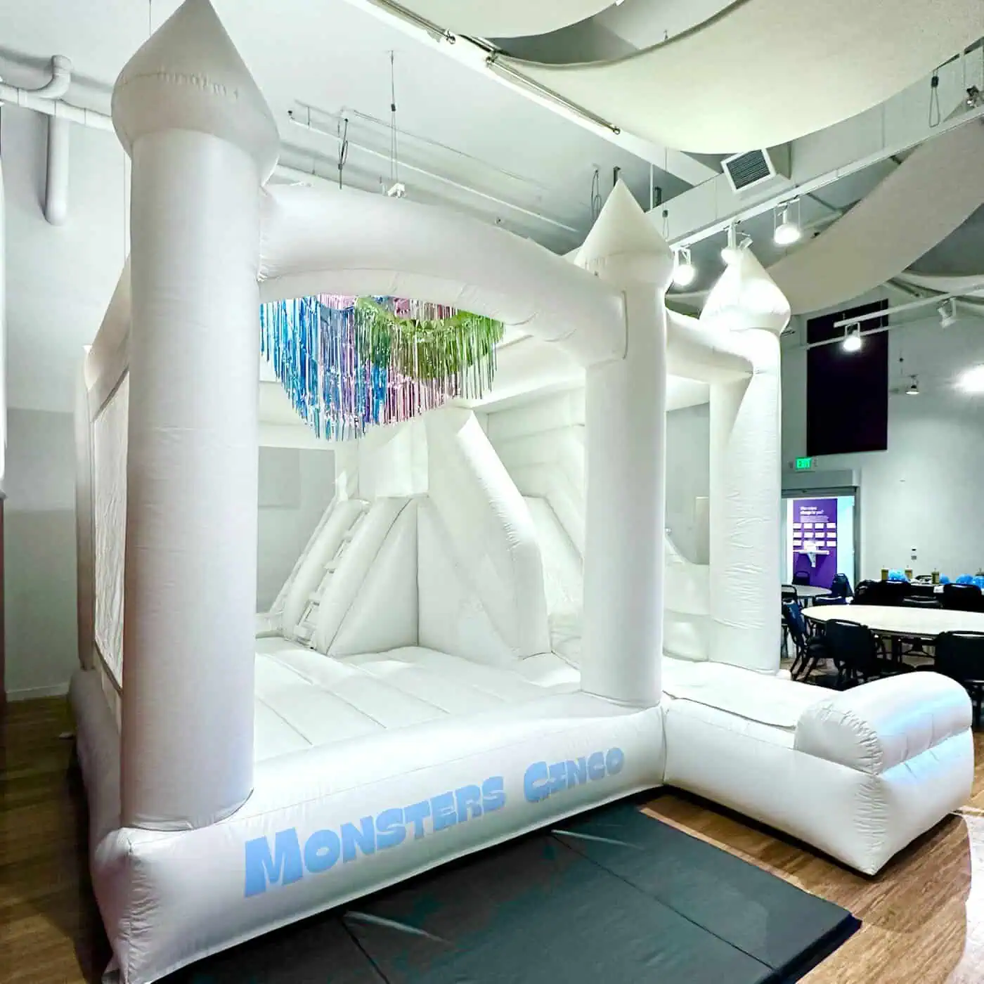 St. Helens white bounce castle with a slide and a custom Monsters Cinco sign, set up indoors at an event space