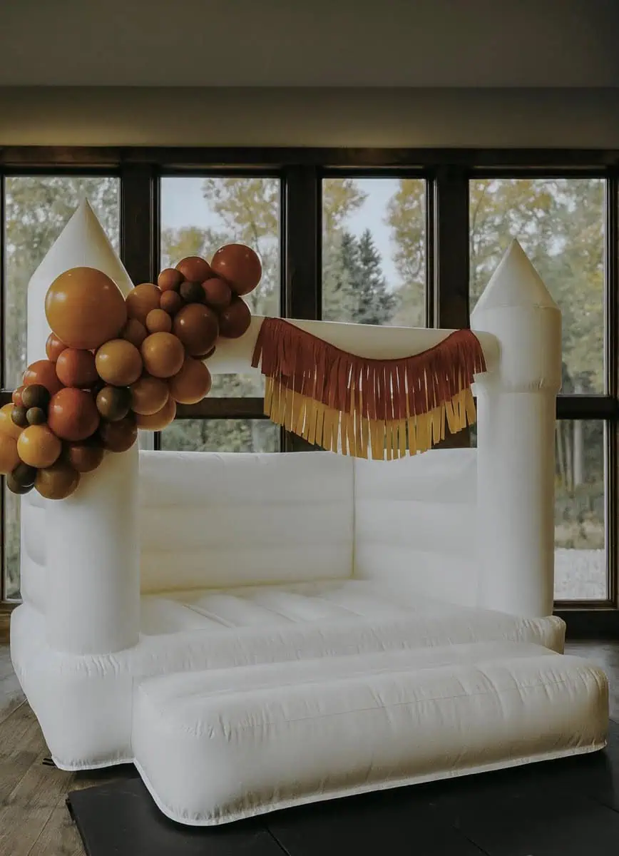 Thaya white bounce castle with a rust, copper and cream balloon garland and fringe for a fall party