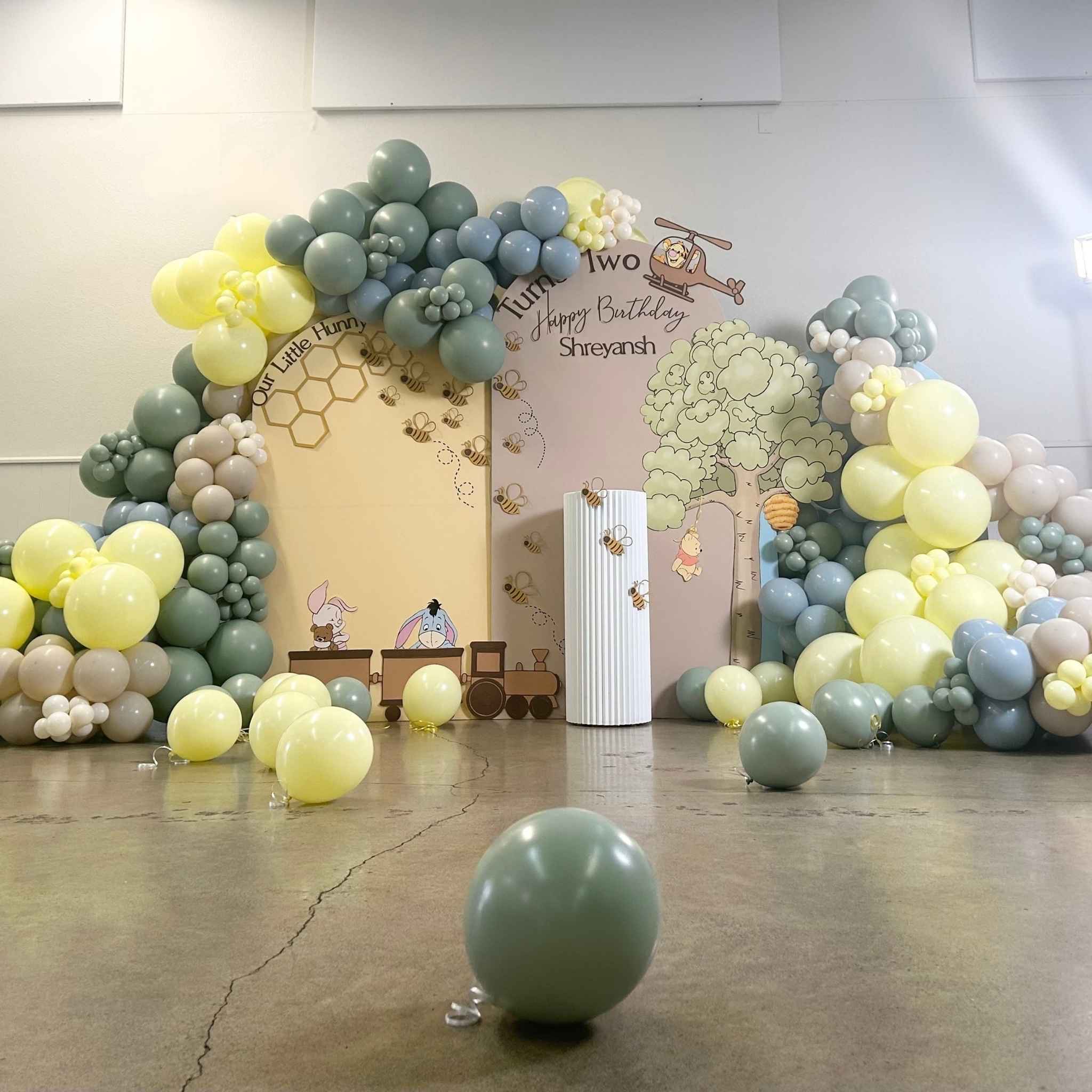 Sage, sand, and yellow balloon garland and Winnie the Pooh backdrop for a second birthday at Bothell Rental Hall in Bothell, WA