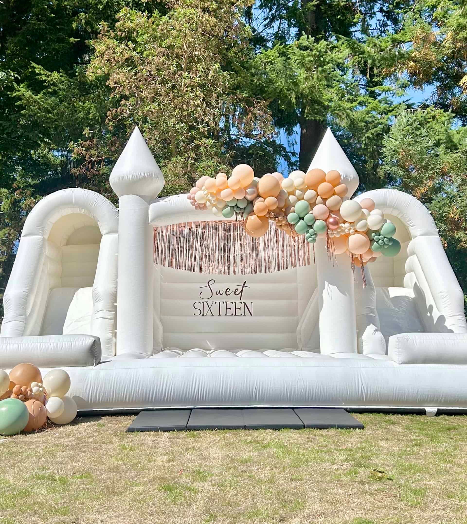 Olympus white bounce house with peach, sage, and ivory balloon garland for a Sweet Sixteen in Monroe, WA