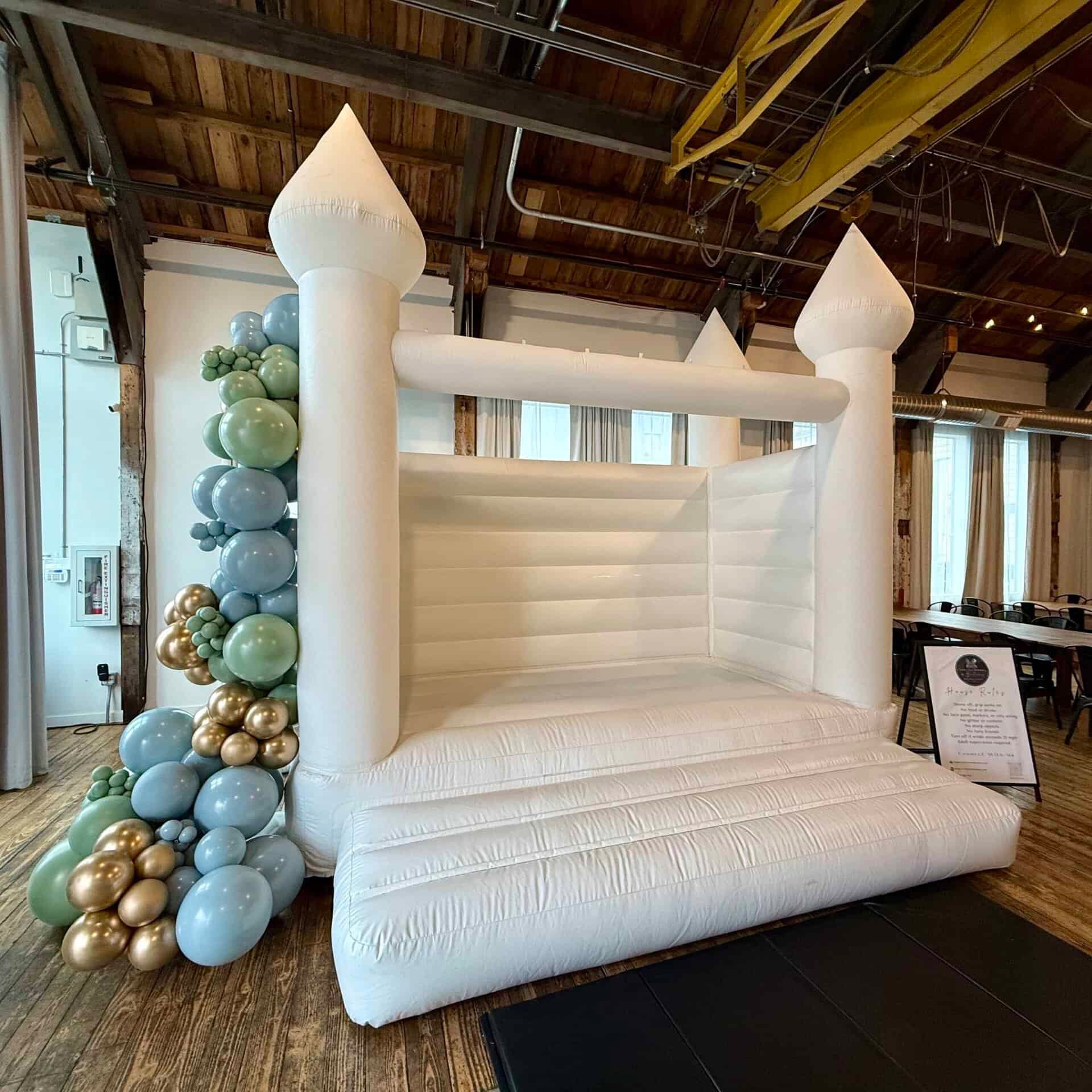 Magnolia white bounce house with powder blue, sage, and gold balloon garland for a wedding in Monroe, WA